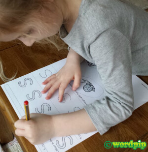 child writing on a letter worksheet on a wooden table