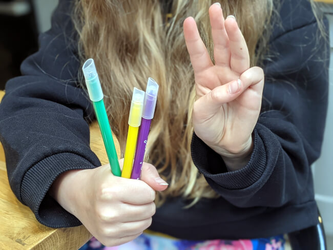 Girl holding 3 coloured pens
